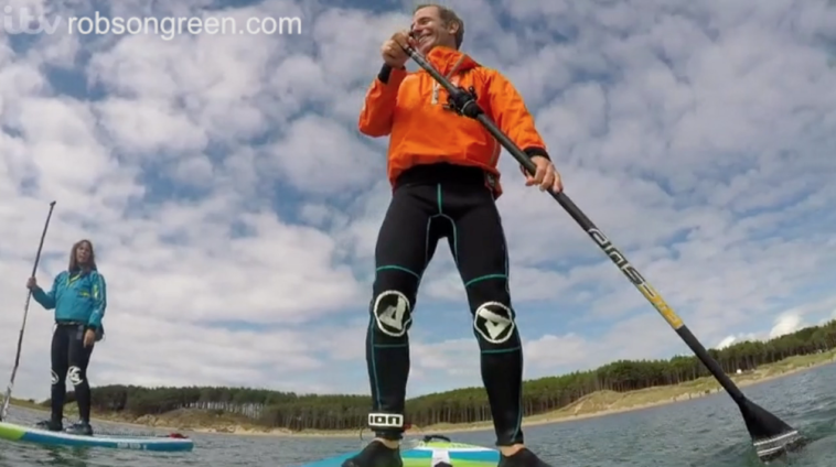 Robson Green is paddle-boarding on the Welsh Isle of Anglesey.
