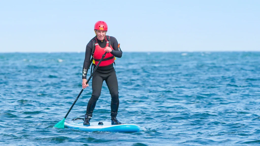 Robson Green wearing a wet suit paddle boarding on the sea