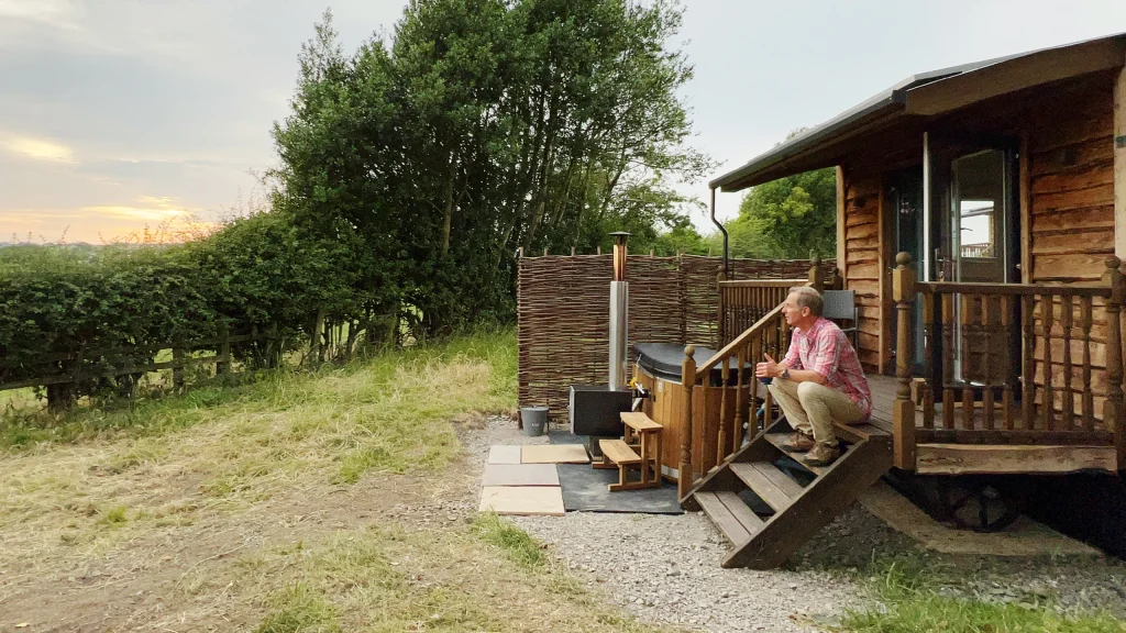 Robson Green sitting on the steps of a holiday lodge looking out over the countryside