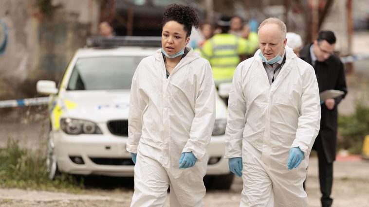 Two people wearing white protective overalls and blue gloves